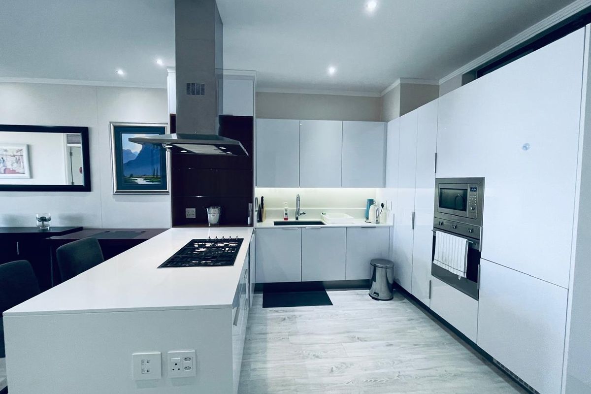 Modern kitchen featuring a central island with gas hob, integrated appliances, sleek white cabinetry, and contemporary finishes.