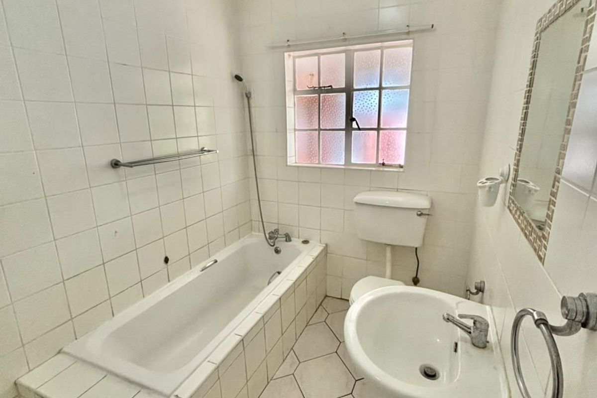 A functional bathroom featuring a built-in bathtub, pedestal sink, and toilet with tiled finishes throughout.