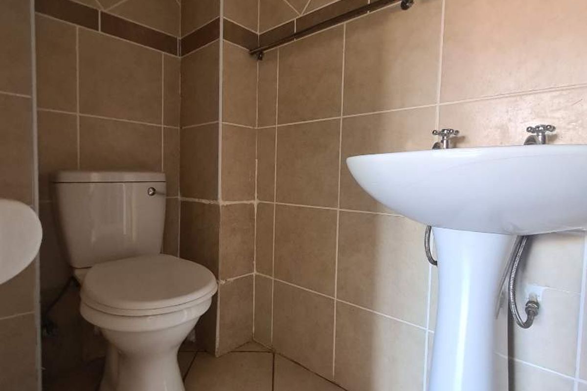 A functional bathroom featuring a pedestal basin, toilet, and neutral tiled finishes throughout.