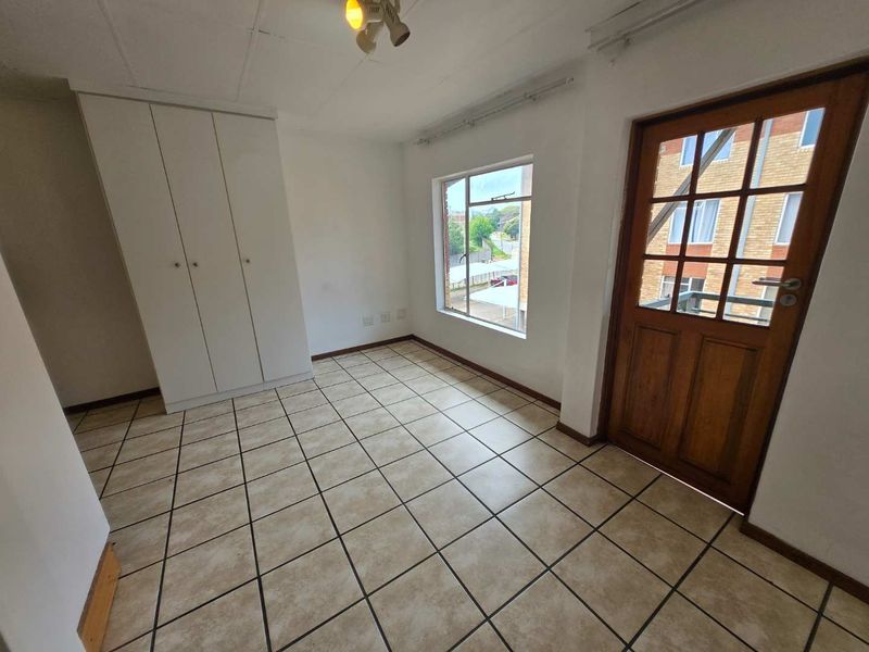 An empty bedroom featuring tiled flooring, a built-in wardrobe, and a timber-framed glass door leading to an exterior balcony.