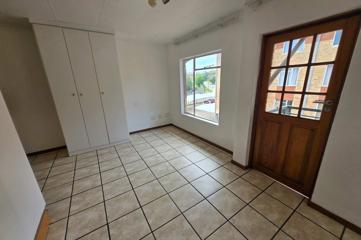 An empty bedroom featuring tiled flooring, a built-in wardrobe, and a timber-framed glass door leading to an exterior balcony.