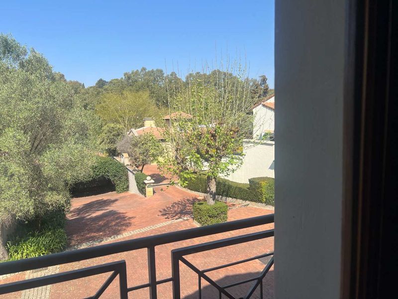 A view from an elevated balcony overlooking a brick-paved driveway and landscaped garden area.