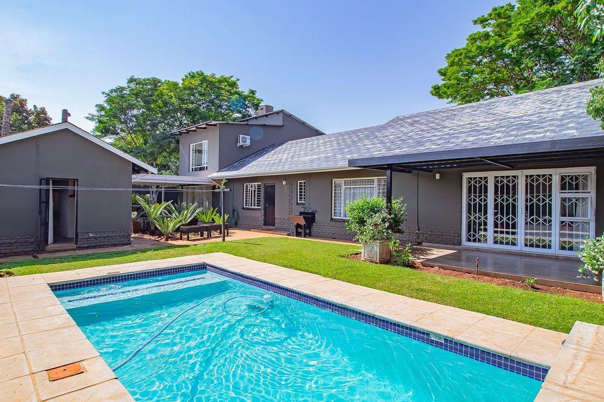 Rear view of the property featuring a swimming pool, paved patio area, and a well-maintained garden with established trees.
