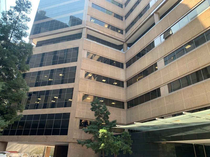 A modern multi-story office building featuring a glass curtain wall facade, tinted windows, and a prominent glass entrance canopy.