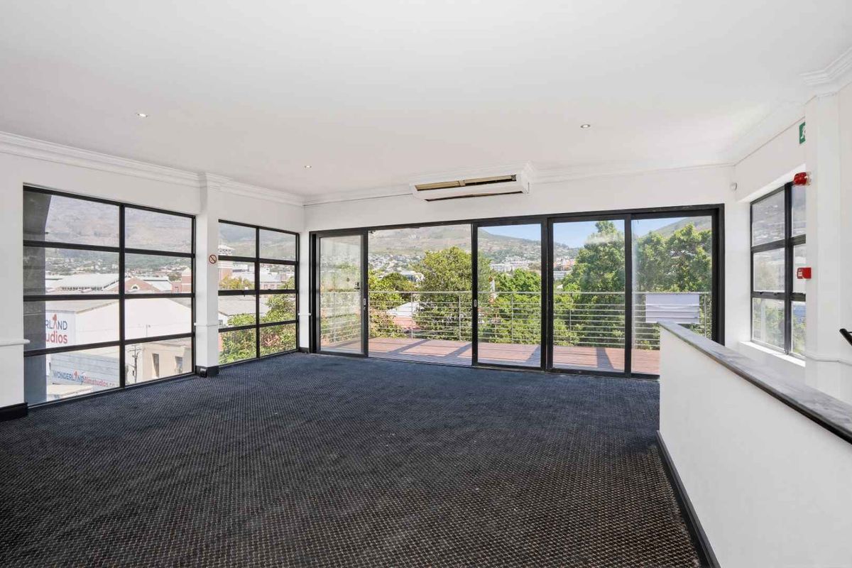 Spacious, light-filled office area featuring large black-framed windows, carpeted flooring, and direct access to a private balcony with scenic views.