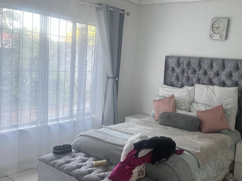 A bedroom featuring tiled flooring and a window fitted with security bars, providing natural light.