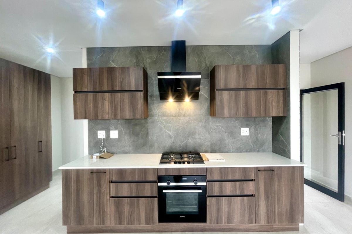 Modern kitchen featuring dark wood cabinetry, stone-look backsplash, built-in oven, gas hob, and sleek extractor fan with contemporary track lighting.