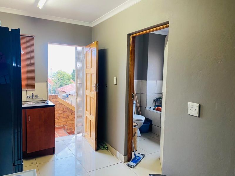 A functional kitchen area featuring tiled floors, built-in cabinetry, and direct access to an outdoor balcony and an adjacent bathroom.