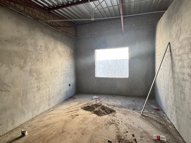 An unfinished room in shell condition featuring exposed steel roof trusses, corrugated metal roofing, and raw cement walls, awaiting final interior finishes.