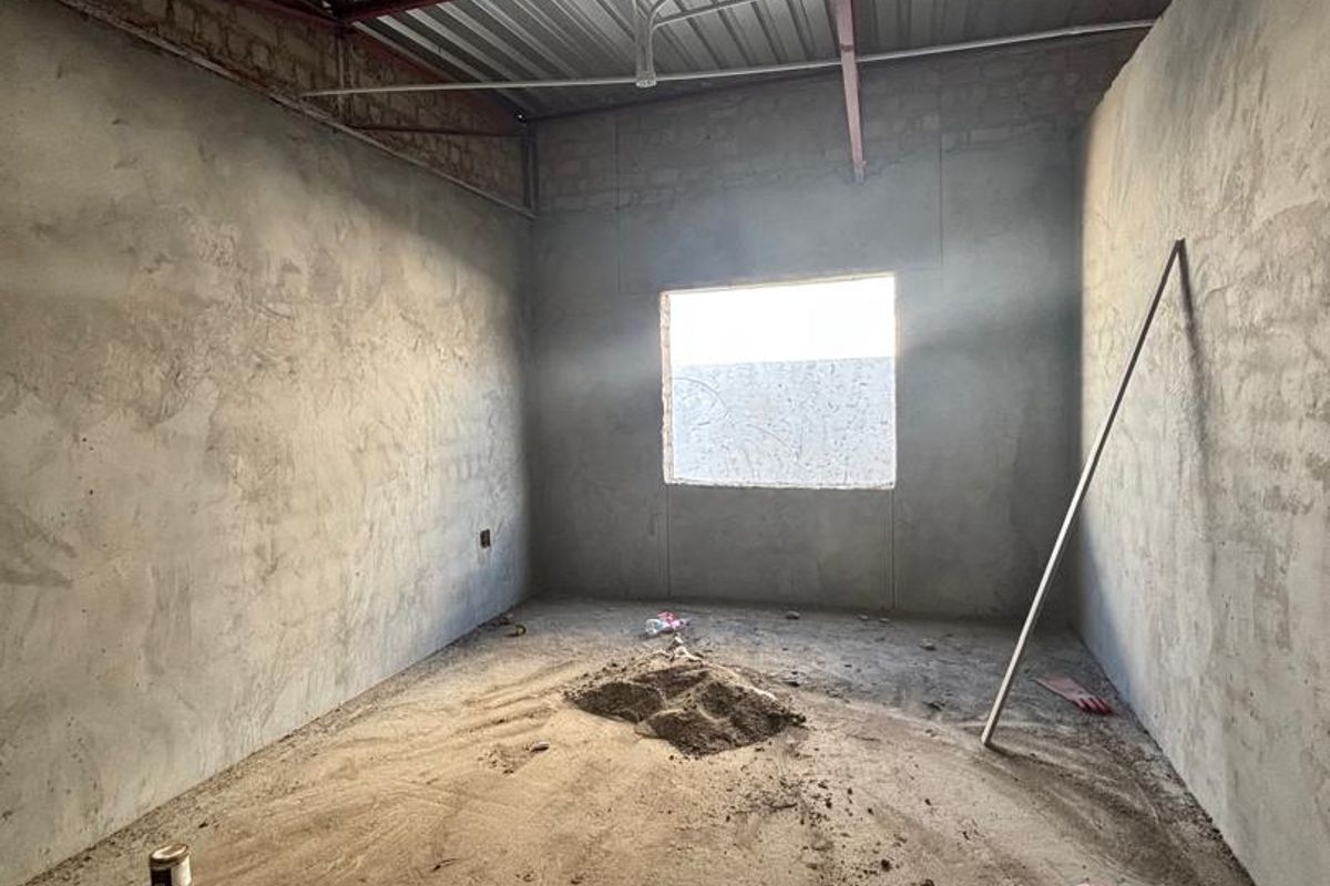 An unfinished room in shell condition featuring exposed steel roof trusses, corrugated metal roofing, and raw cement walls, awaiting final interior finishes.