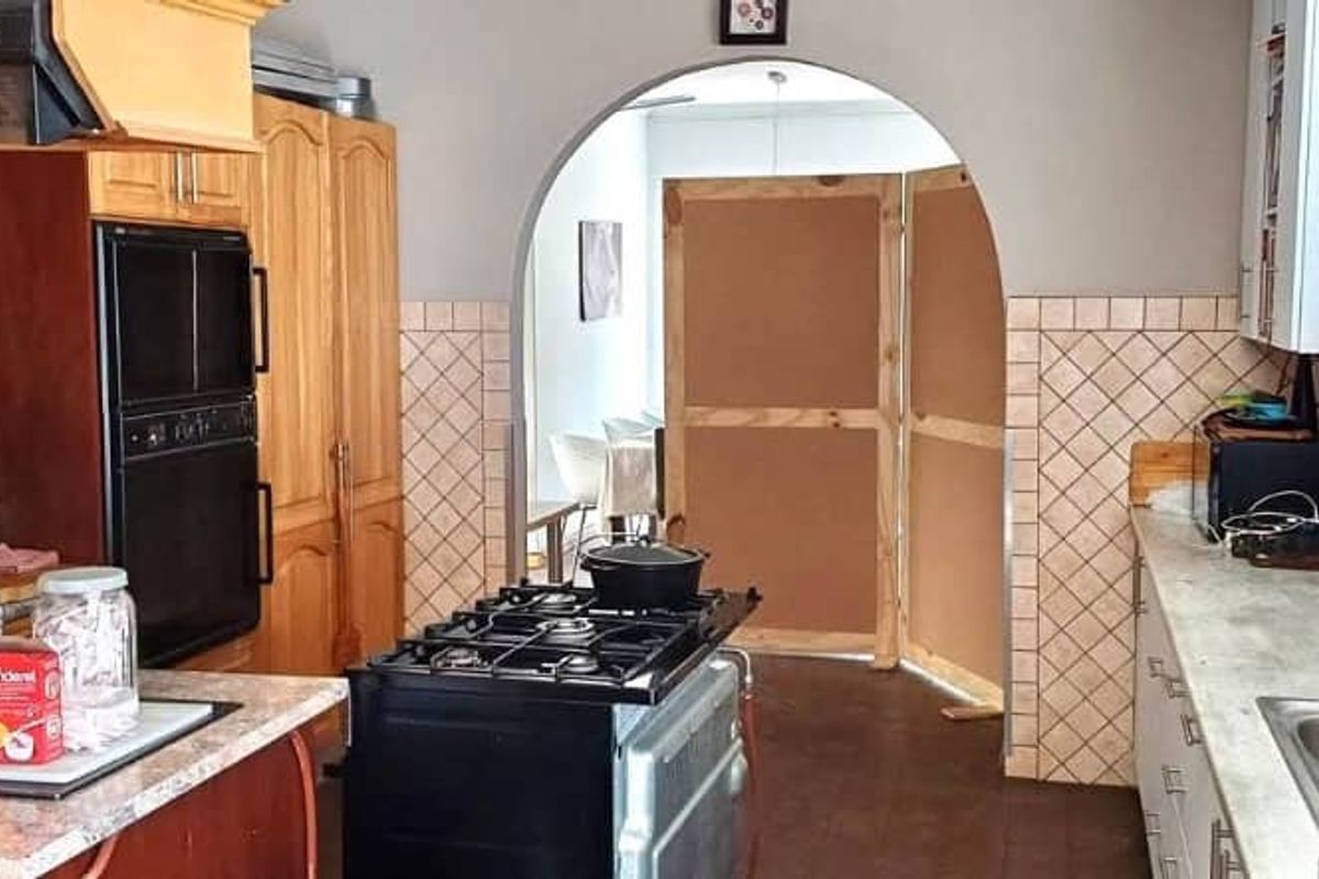 A functional kitchen featuring wooden cabinetry, a built-in oven, a gas hob, and a tiled backsplash, leading through an arched doorway to adjacent living space.