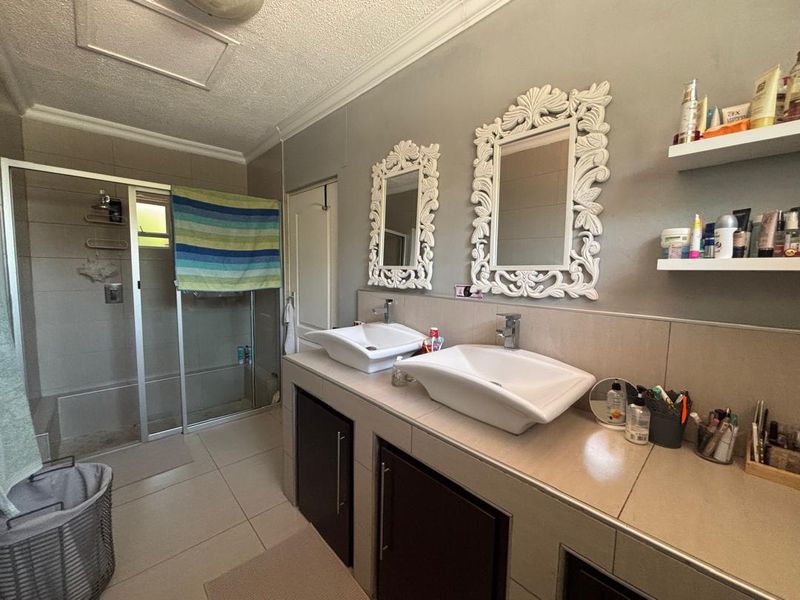 A functional bathroom featuring a double vanity with vessel sinks, a glass-enclosed shower, and neutral wall tiling.