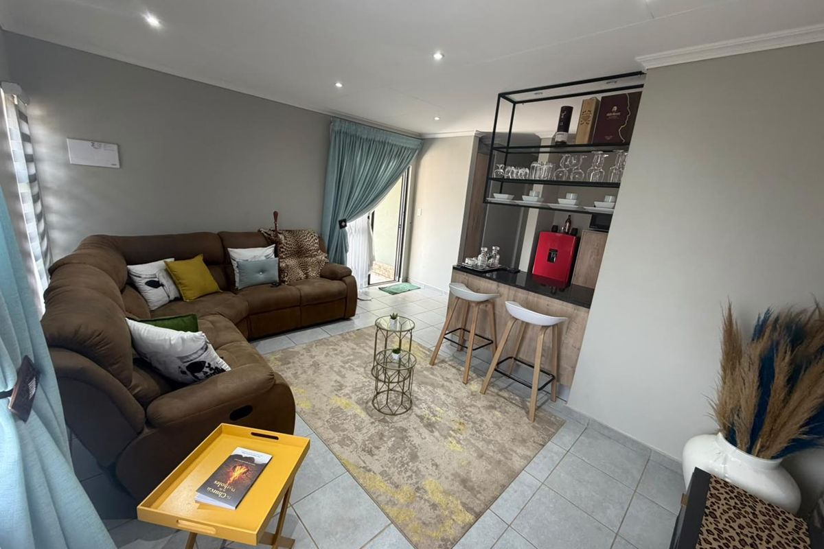 A well-maintained living room featuring tiled floors, recessed lighting, and a built-in bar area with shelving, leading to an outdoor space.