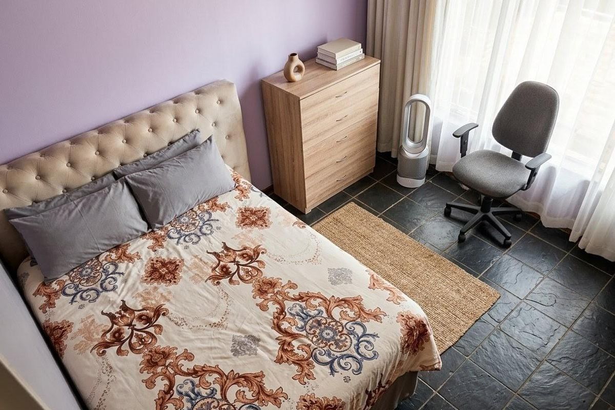 A bedroom featuring dark slate tile flooring and a large window with sheer curtains, providing natural light to the space.