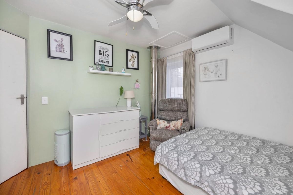 A bedroom featuring polished timber flooring, a ceiling fan, and a wall-mounted air conditioning unit.