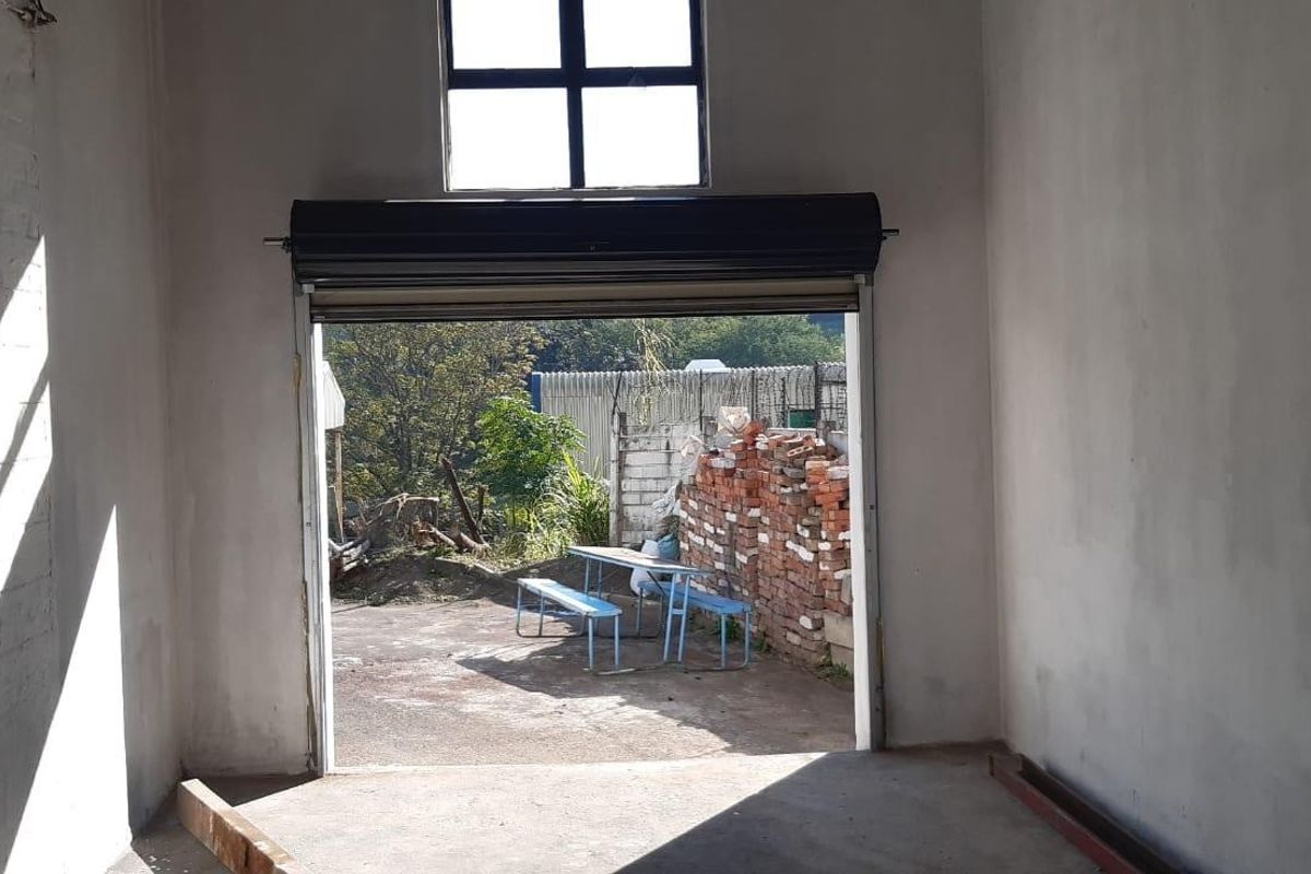 An empty industrial utility space featuring a roller shutter door, high-level window, and unfinished wall surfaces, suitable for storage or workshop use.