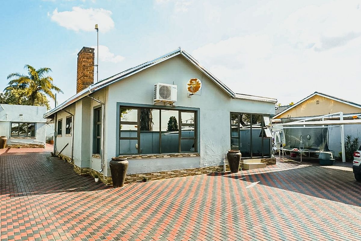 Rear view of the property featuring a paved driveway, brick chimney, and exterior air conditioning unit.