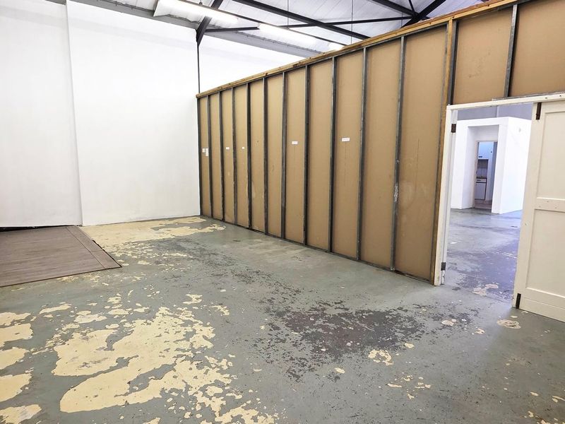 An industrial utility space featuring exposed roof trusses, concrete flooring with significant wear, and unfinished partition walling, offering a blank canvas for renovation.