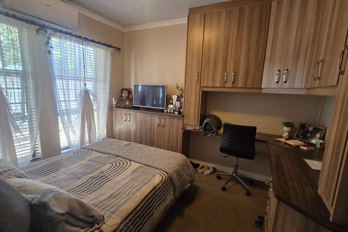A well-maintained bedroom featuring extensive built-in cabinetry, a dedicated desk area, and a wall-mounted air conditioning unit.