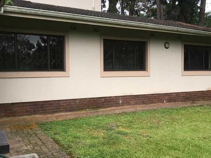 Rear exterior view of the townhouse featuring a brick plinth, tiled roof, and paved walkway leading along the back facade.