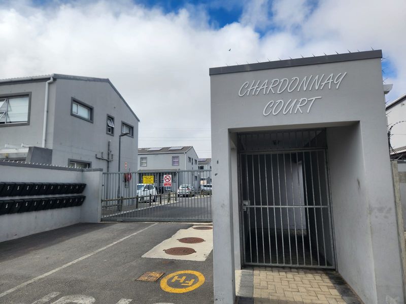 The entrance to Chardonnay Court featuring a secure gated access point, perimeter wall with security spikes, and a paved driveway.