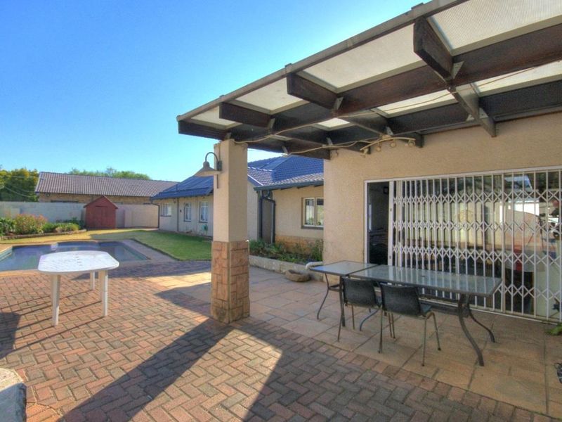 A covered outdoor patio area featuring brick paving, a stone-clad pillar, and direct access to the swimming pool and garden.