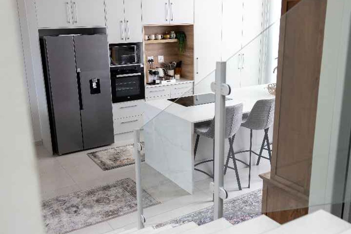 Modern open-plan kitchen featuring sleek white cabinetry, a central island with stone countertops, and integrated appliances, viewed from the staircase.