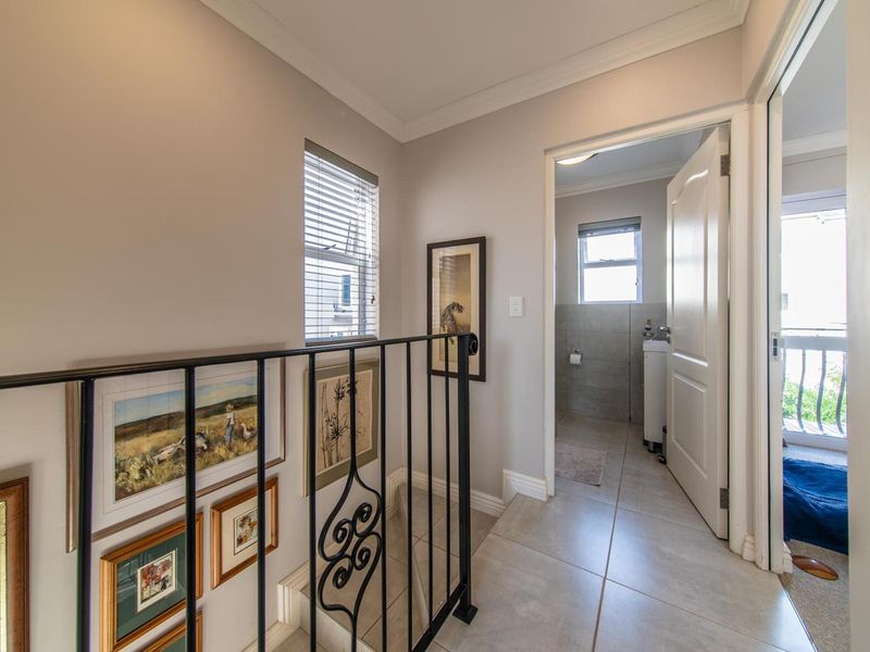 A bright hallway featuring tiled flooring, a decorative wrought iron balustrade, and access to an adjacent bathroom.