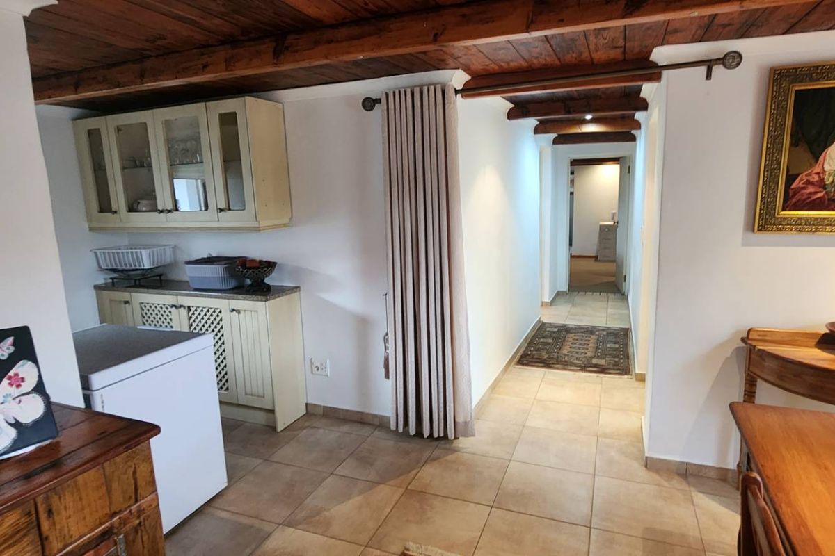 Kitchen area featuring exposed timber ceiling beams, tiled flooring, and built-in cabinetry, leading into a hallway.