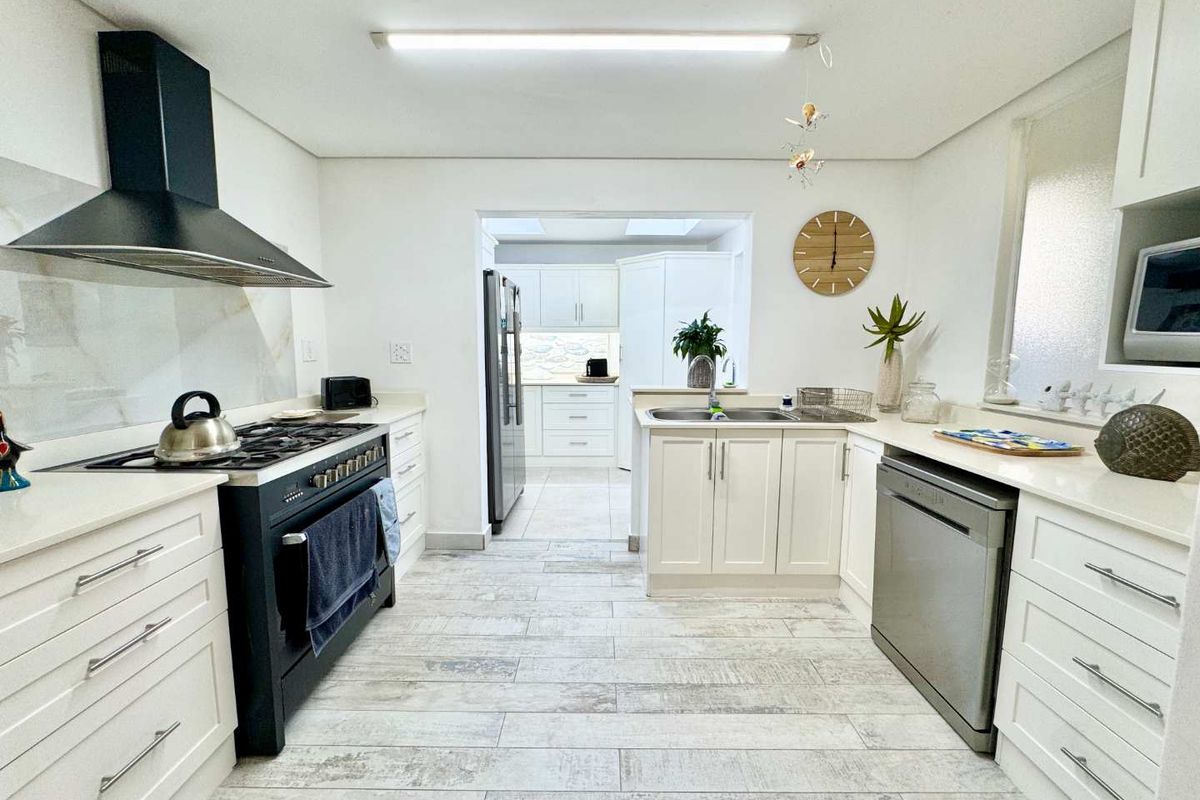 Modern kitchen featuring white cabinetry, stone countertops, a gas hob with extractor fan, and a secondary scullery area visible in the background.