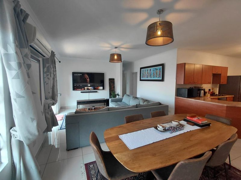 Open-plan living and dining area featuring tiled floors, split-system air conditioning, and an adjoining kitchen with wooden cabinetry.