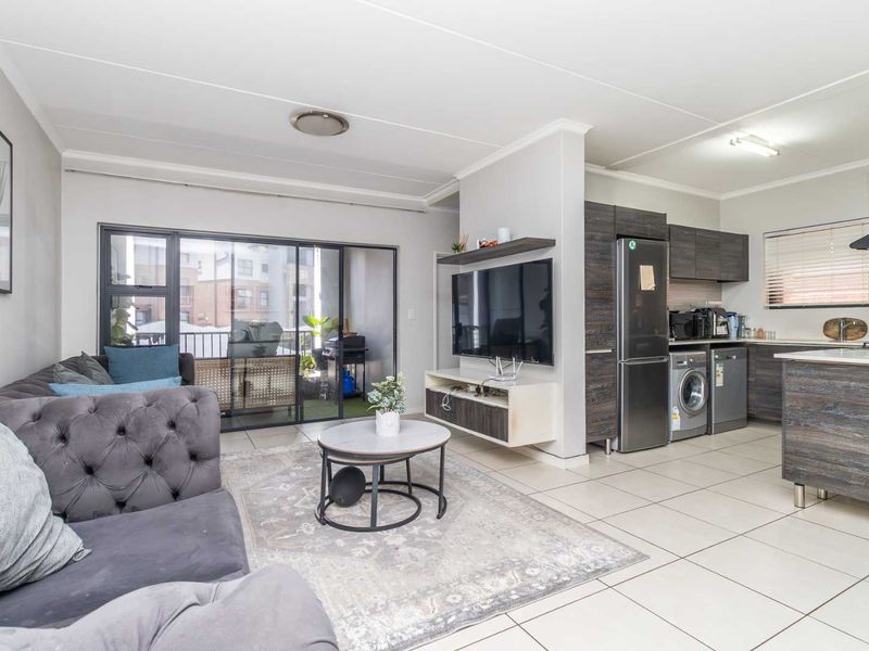Modern open-plan living area featuring tiled floors, a contemporary kitchen with built-in cabinetry, and seamless access to a private balcony through sliding glass doors.