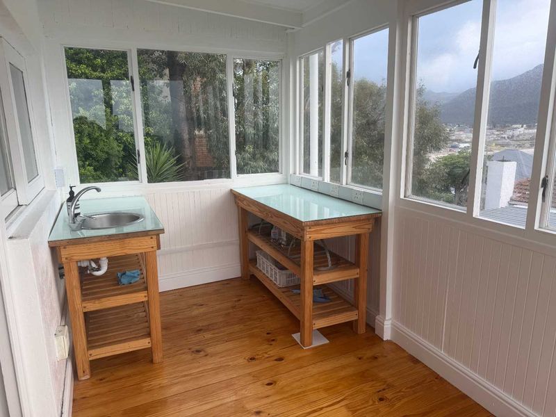A bright, sunlit scullery or utility area featuring timber cabinetry, a stainless steel sink, and expansive windows with scenic views.