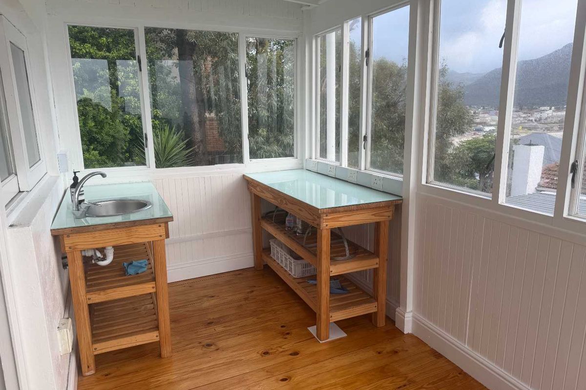 A bright, sunlit scullery or utility area featuring timber cabinetry, a stainless steel sink, and expansive windows with scenic views.
