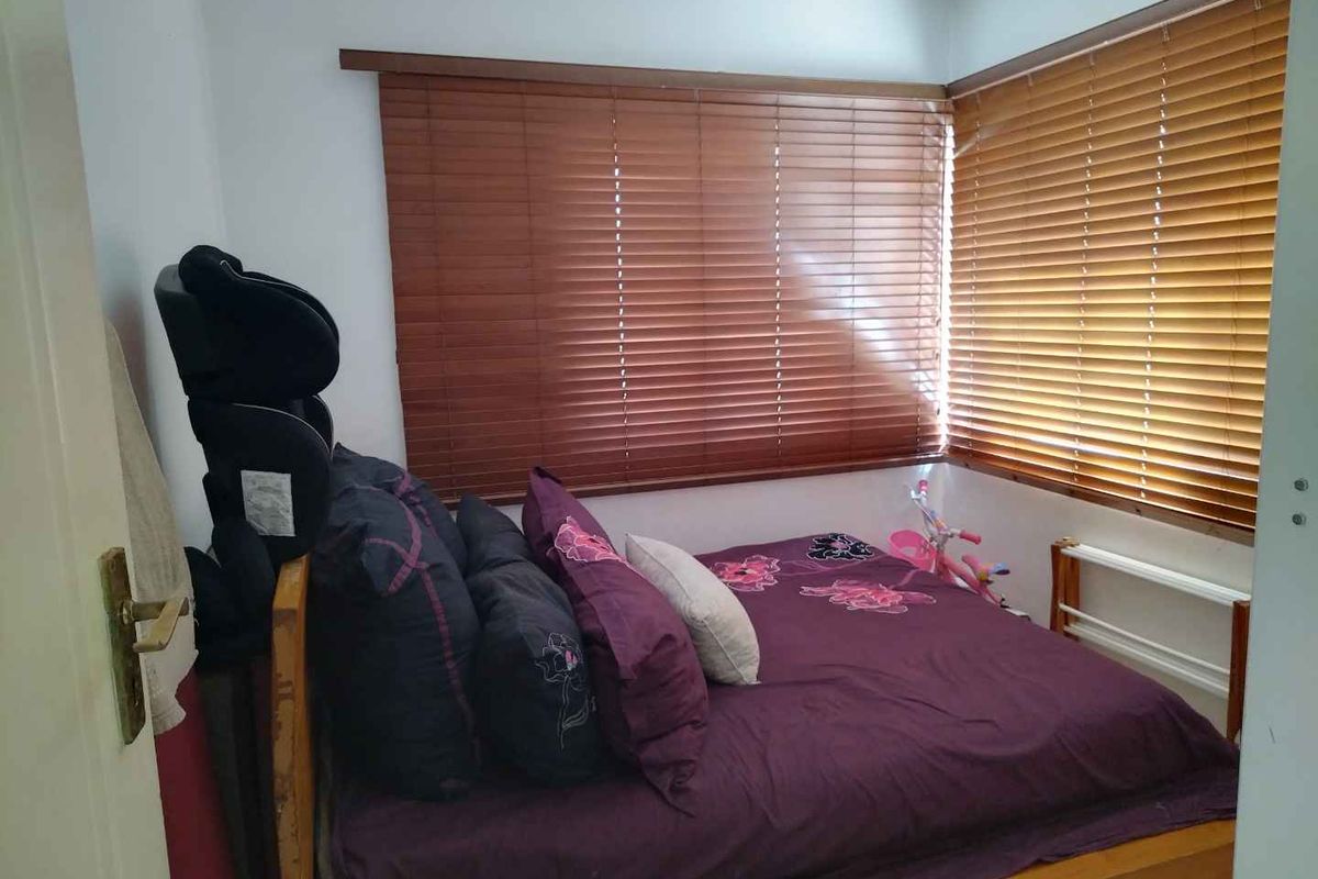 A compact bedroom featuring wooden venetian blinds and neutral wall finishes, offering a functional space for rest.