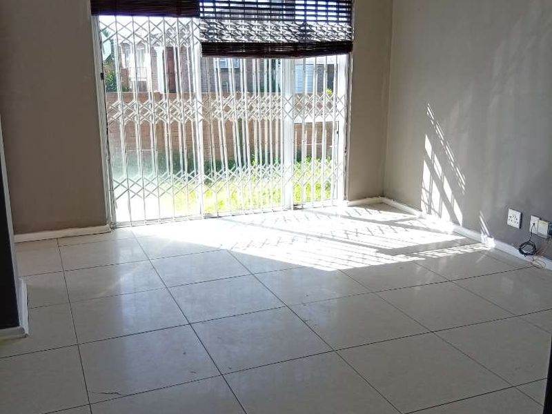 An empty living room featuring neutral tiled flooring, grey walls, and a sliding glass door with a security gate leading to the exterior.