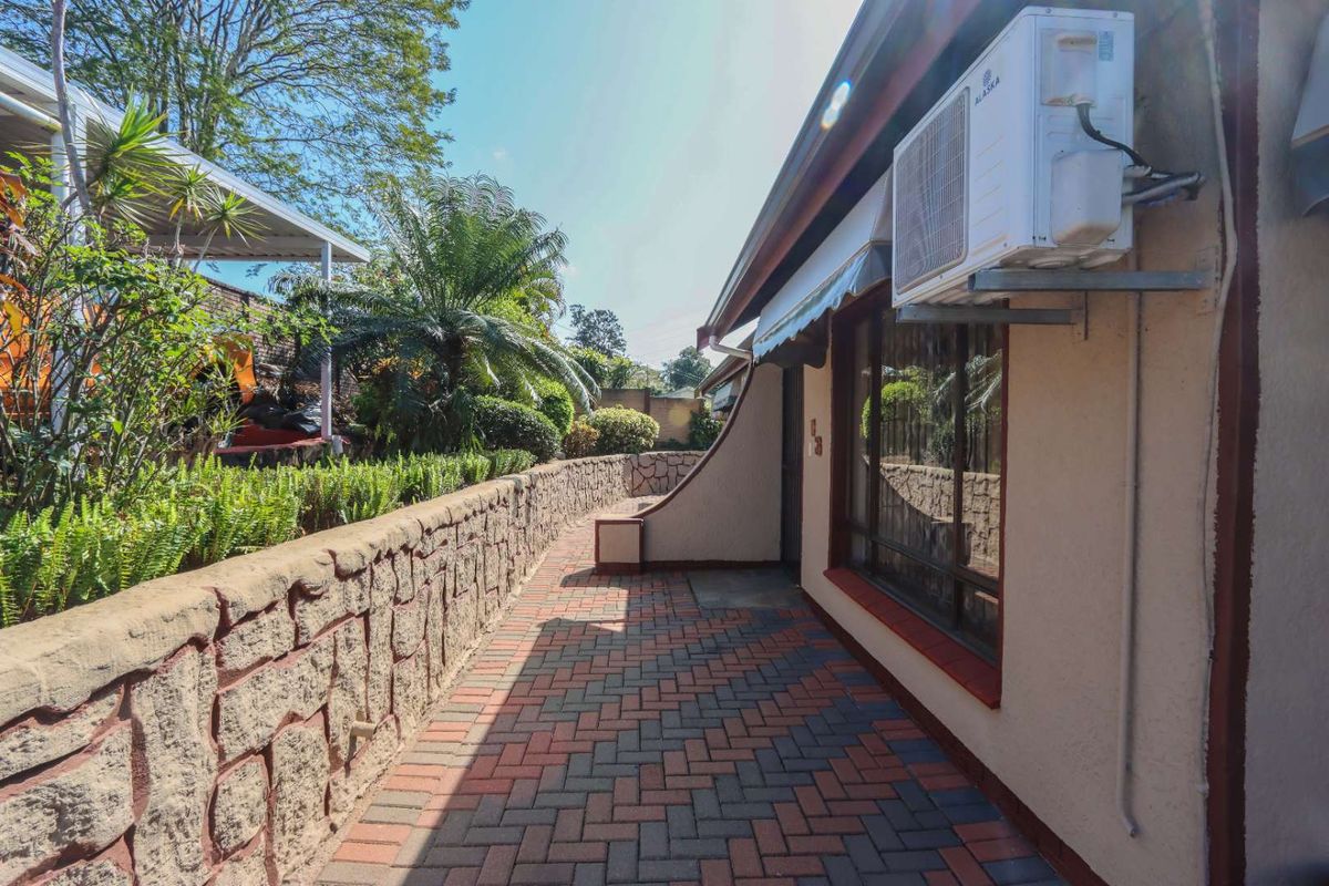 A paved side walkway featuring a stone retaining wall, exterior air conditioning unit, and access to the garden area.