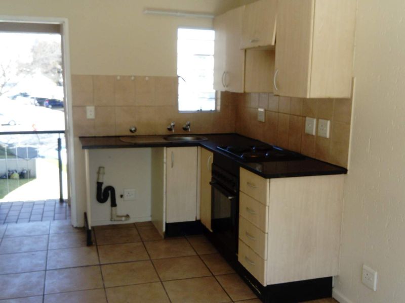 A compact kitchen featuring light-toned cabinetry, dark countertops, a built-in oven and hob, and tiled flooring, with direct access to an outdoor balcony.