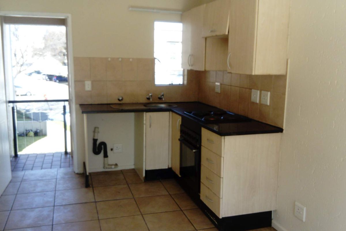 A compact kitchen featuring light-toned cabinetry, dark countertops, a built-in oven and hob, and tiled flooring, with direct access to an outdoor balcony.