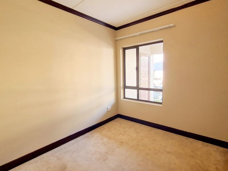 A clean, empty bedroom featuring neutral walls, dark wood-tone skirting boards, and an aluminium-framed window.