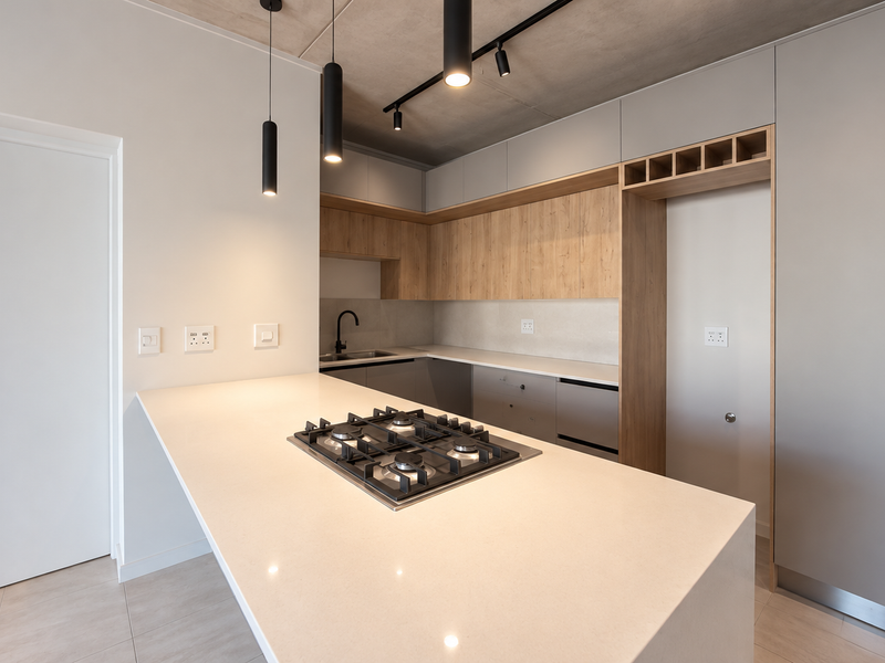 Modern kitchen featuring a central island with a gas hob, stone countertops, sleek cabinetry, and contemporary pendant lighting against an exposed concrete ceiling.