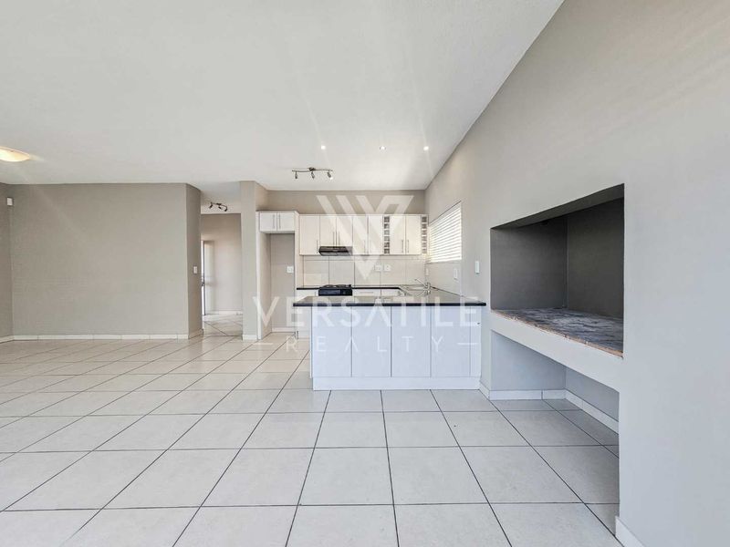 Spacious open-plan living area featuring a modern kitchen with built-in cabinetry and a dedicated indoor braai area, finished with neutral floor tiles.