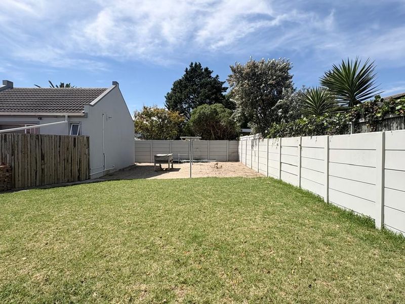 A spacious rear garden featuring a lawn area, precast concrete boundary walls, and a timber fence, offering potential for landscaping and outdoor living.