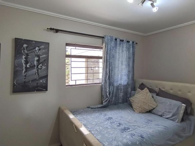 A functional bedroom featuring a window with security bars, neutral wall finishes, and a ceiling-mounted light fixture.
