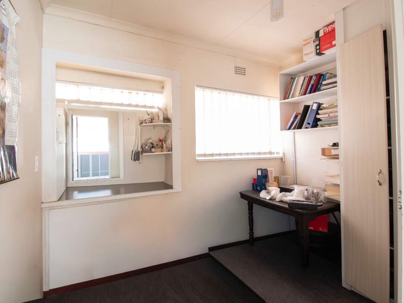 A functional home office space featuring built-in shelving, a built-in cupboard, and an internal window providing natural light.