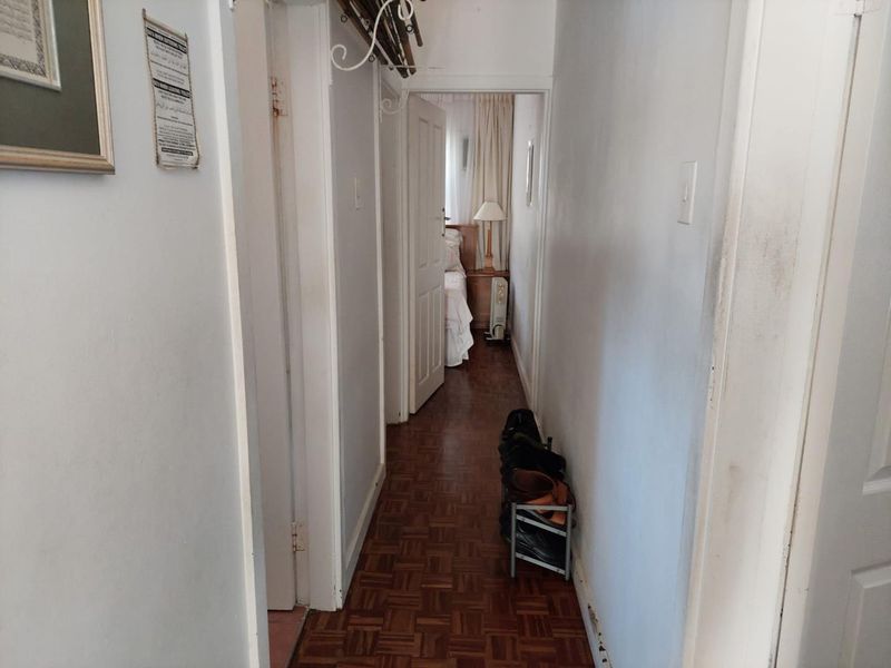 A narrow residential hallway featuring traditional parquet flooring and access to adjacent rooms, showing signs of wear and requiring cosmetic updates.