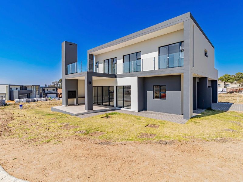 Modern double-story residence featuring a rear patio with a built-in braai, glass balustrades on the upper balcony, and large sliding doors.