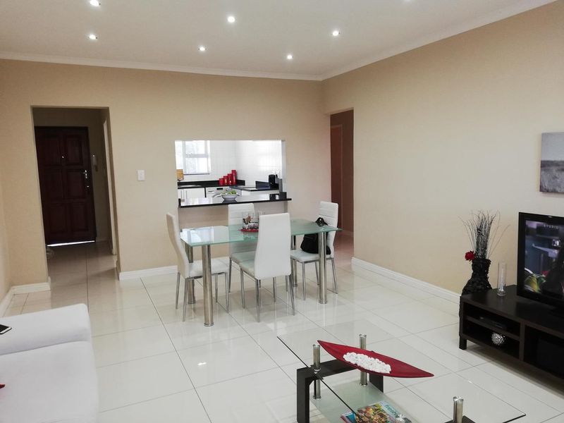 Open-plan living and dining area featuring neutral walls, tiled flooring, recessed lighting, and a convenient pass-through window connecting to the kitchen.
