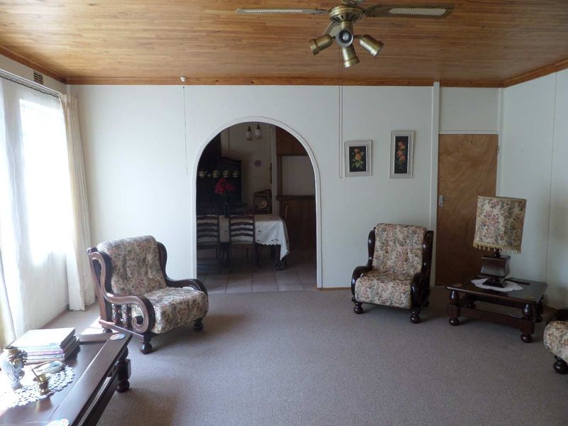 A living room featuring a timber ceiling, ceiling fan, and an arched doorway leading to an adjacent dining area.