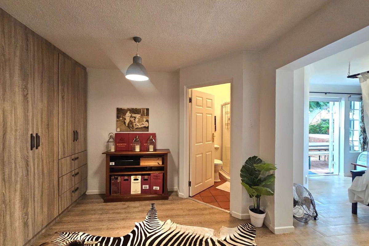 A bedroom featuring built-in wooden cabinetry, laminate flooring, and an en-suite bathroom, with a seamless transition to an adjacent living area.